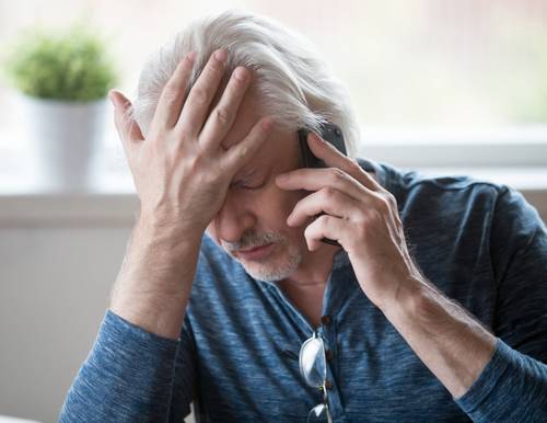 Photo of an older man on the phone with his head in his hand looking depressed